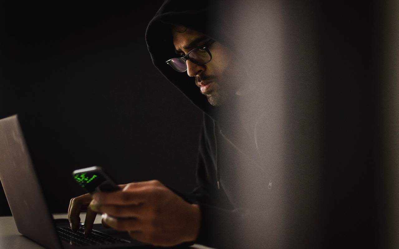 Mutmaßlicher Betrüger mit Handy in der Hand am Laptop