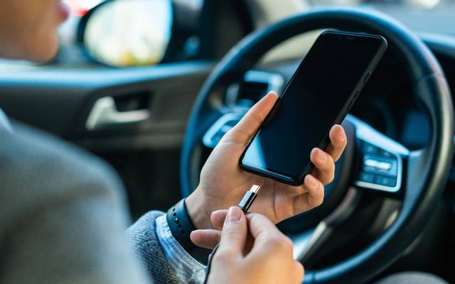 Im Auto wird im Stand ein Handy an ein Ladekabel angeschlossen.