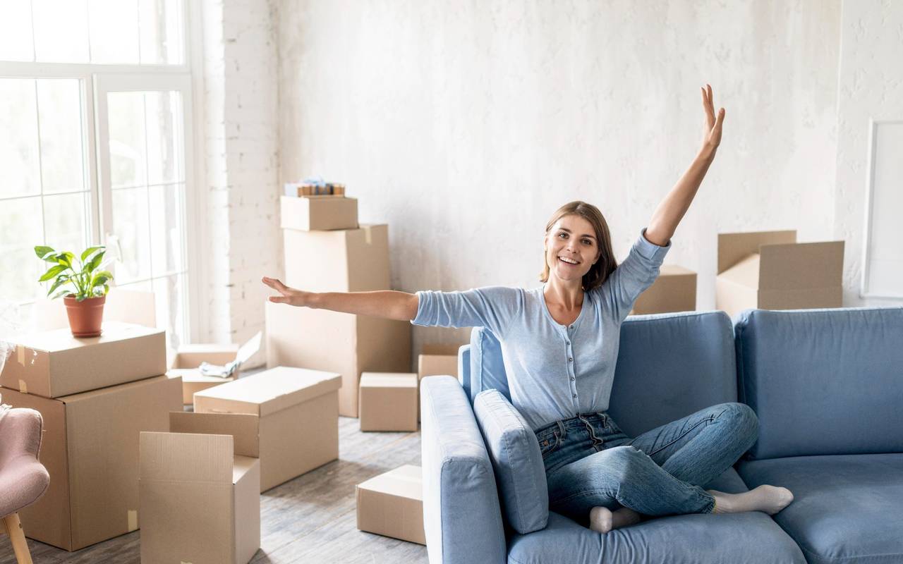 Eine Frau sitzt auf einer Couch in einer frisch bezogenen Wohnung, die noch nicht fertig eingerichtet ist. (Symbolbild)