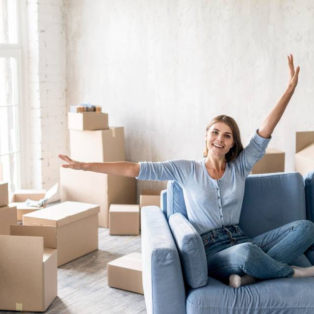Eine Frau sitzt auf einer Couch in einer frisch bezogenen Wohnung, die noch nicht fertig eingerichtet ist. (Symbolbild)