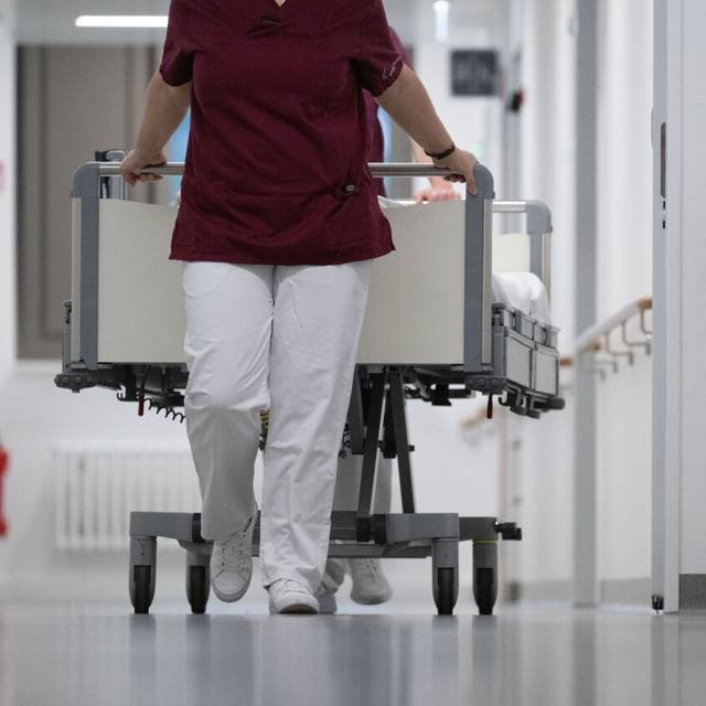 In einem Krankenhaus schiebt eine Krankenschwester ein Bett vor sich her.
