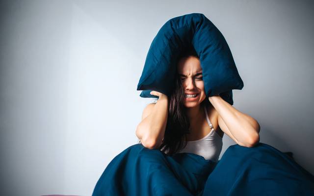 Frau hält sich die Ohren zu und sitzt im Bett
