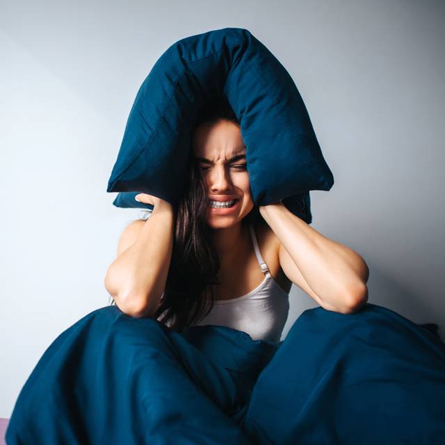 Frau hält sich die Ohren zu und sitzt im Bett