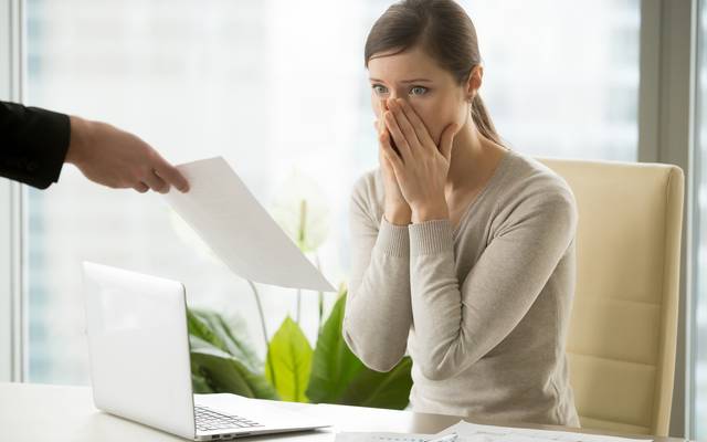 Frau sitzt am Schreibtisch mit geschocktem Gesicht, erhält die Kündigung.