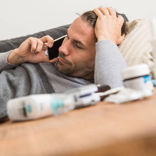 Mann liegt krank auf einem Sofa und telefoniert