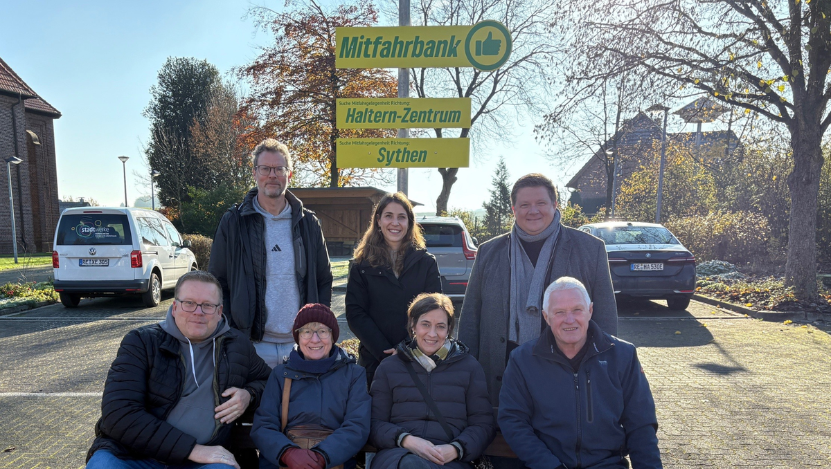 Mehrere Menschen sitzen auf einer Bank in Haltern-Lavesum, darüber ein Schild mit der Aufschrift 'Mitfahrbank' 