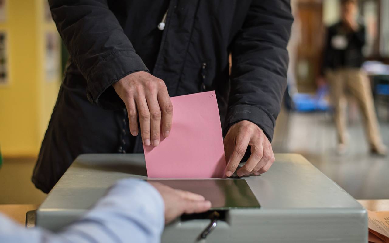 Ein Wahlzettel wird in eine Wahlurne gesteckt.