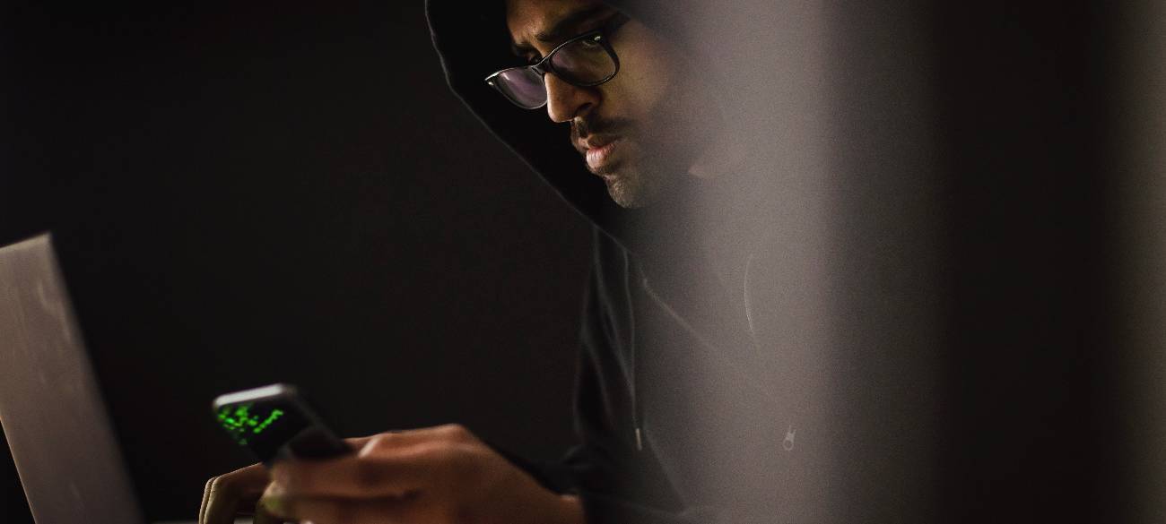 Mutmaßlicher Betrüger mit Handy in der Hand am Laptop