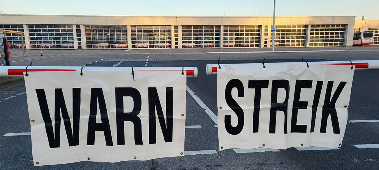 An einem Bus-Betriebshof wird der Warnstreik mit Schildern an einer Schranke verkündet.