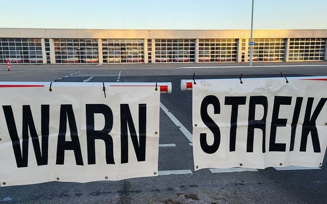 An einem Bus-Betriebshof wird der Warnstreik mit Schildern an einer Schranke verkündet.