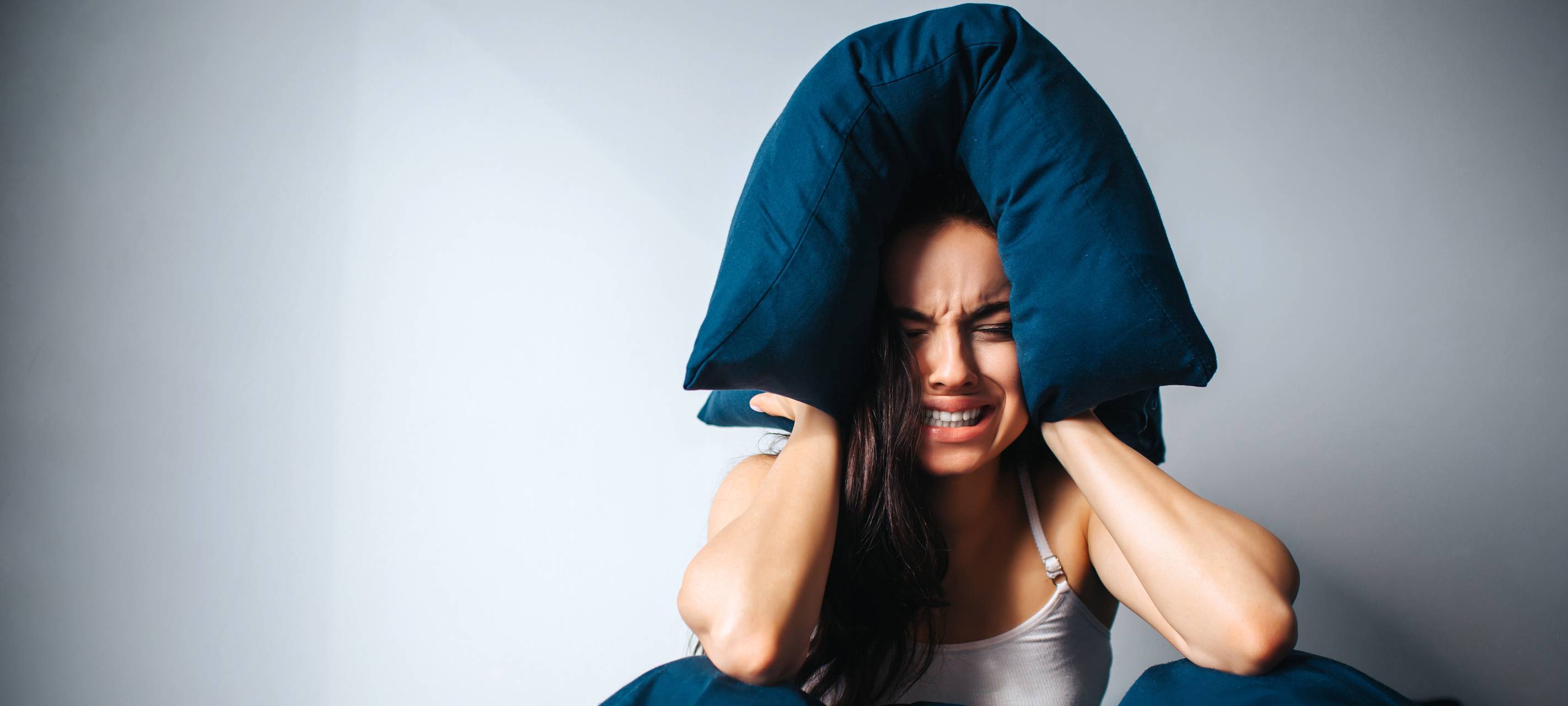 Frau hält sich die Ohren zu und sitzt im Bett