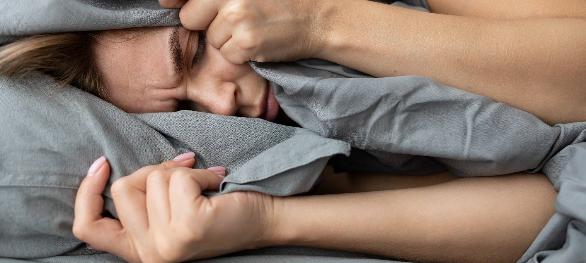 Frau liegt im Bett und hält sich die Decke über die Ohren