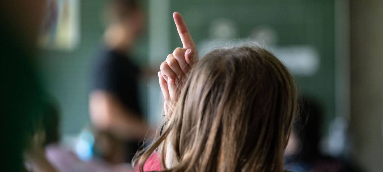 Schülerinnen und Schüler einer vierten Klasse einer Grundschule nehmen am Unterricht teil, eine Schülerin meldet sich.