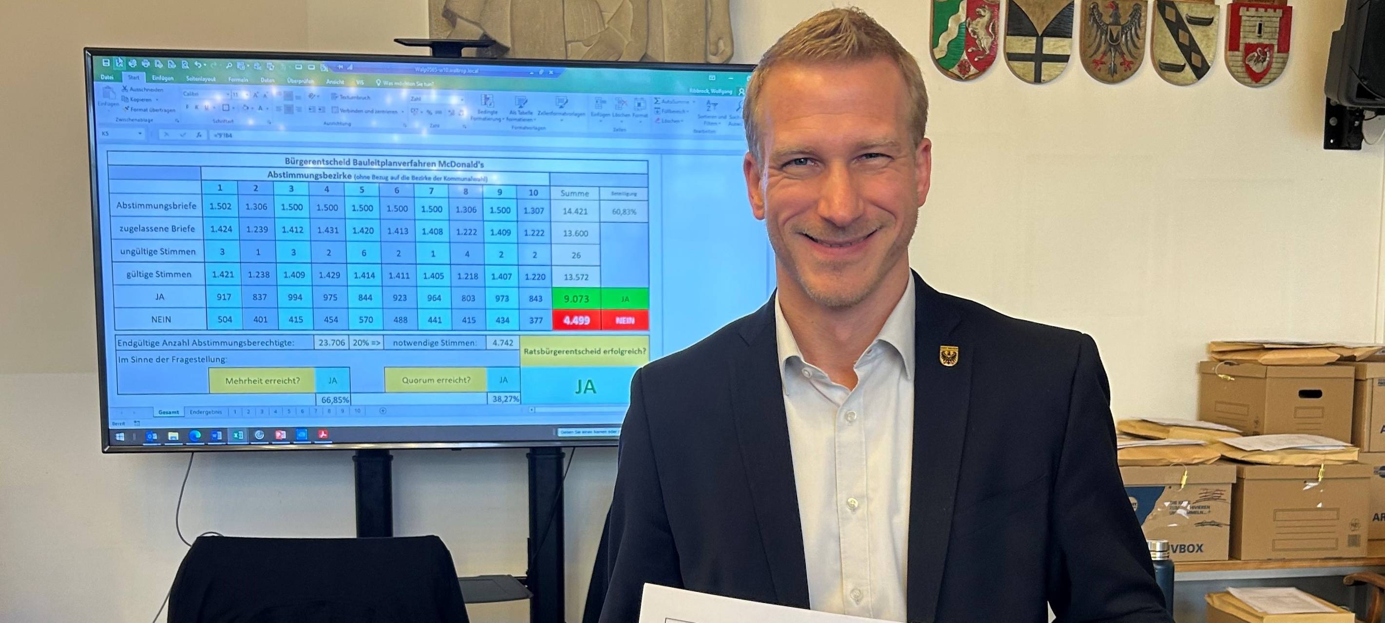 Waltrops Kämmerer Stefan Wilke steht vor einer Leinwand, auf dem das Ergebnis des Entscheids zu sehen ist. Gleichzeitig hält er einen Zettel in der Hand.