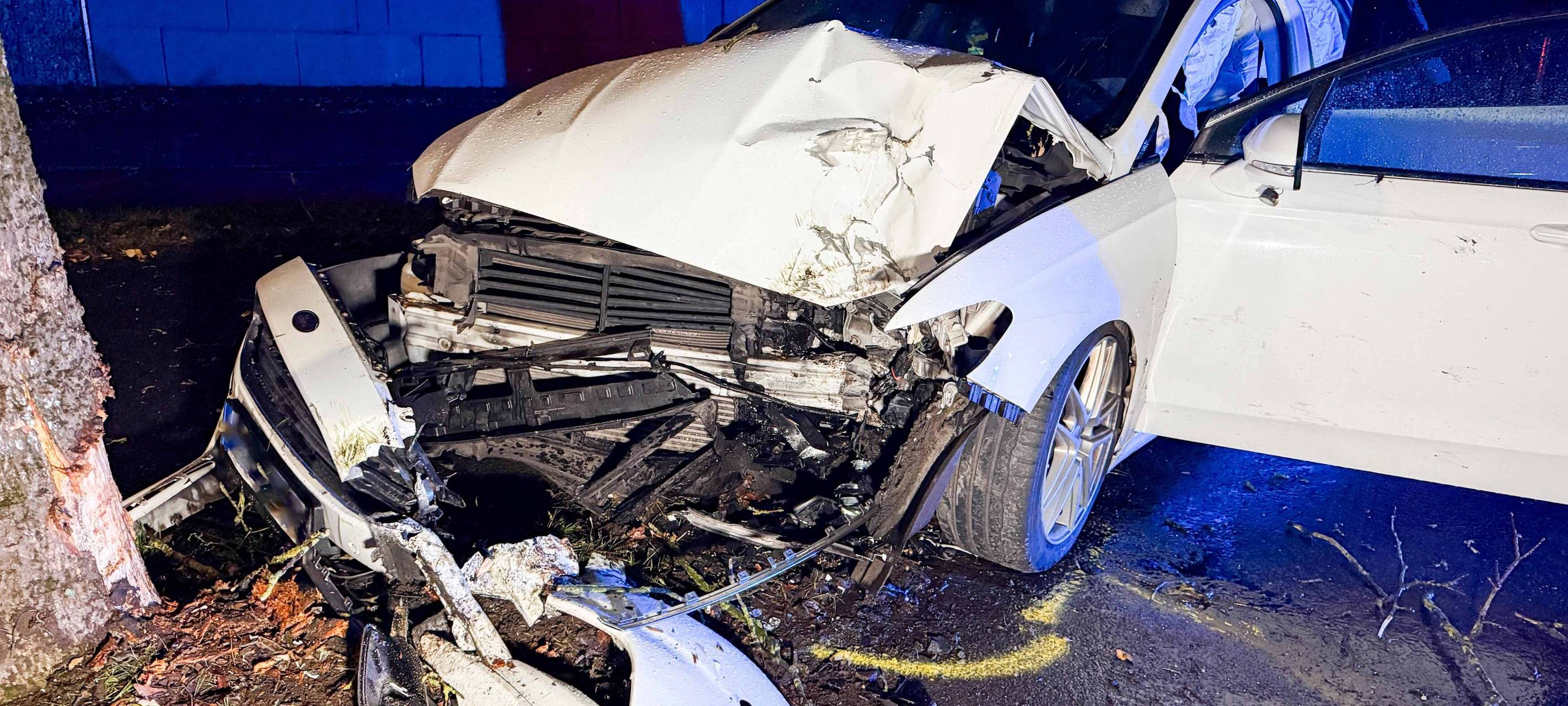 Ein weißes Auto ist vor einen Baum geprallt und an der Front komplett zerstört
