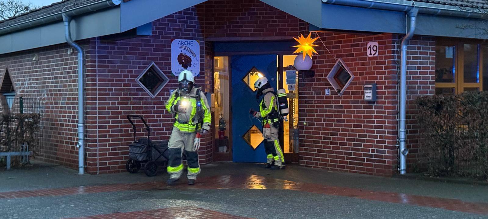 Zwei Feuerwehrleute stehen in Dorsten in Schutzanzügen vor der Kita Arche.