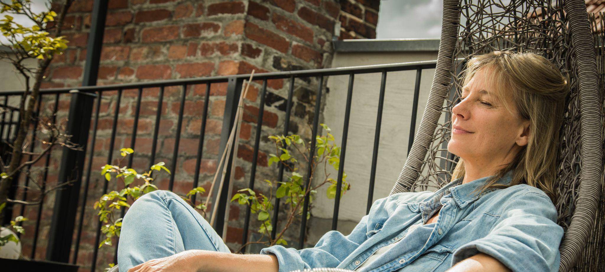 Frau sitzt entspannt im Hängesessel auf einer Terrasse
