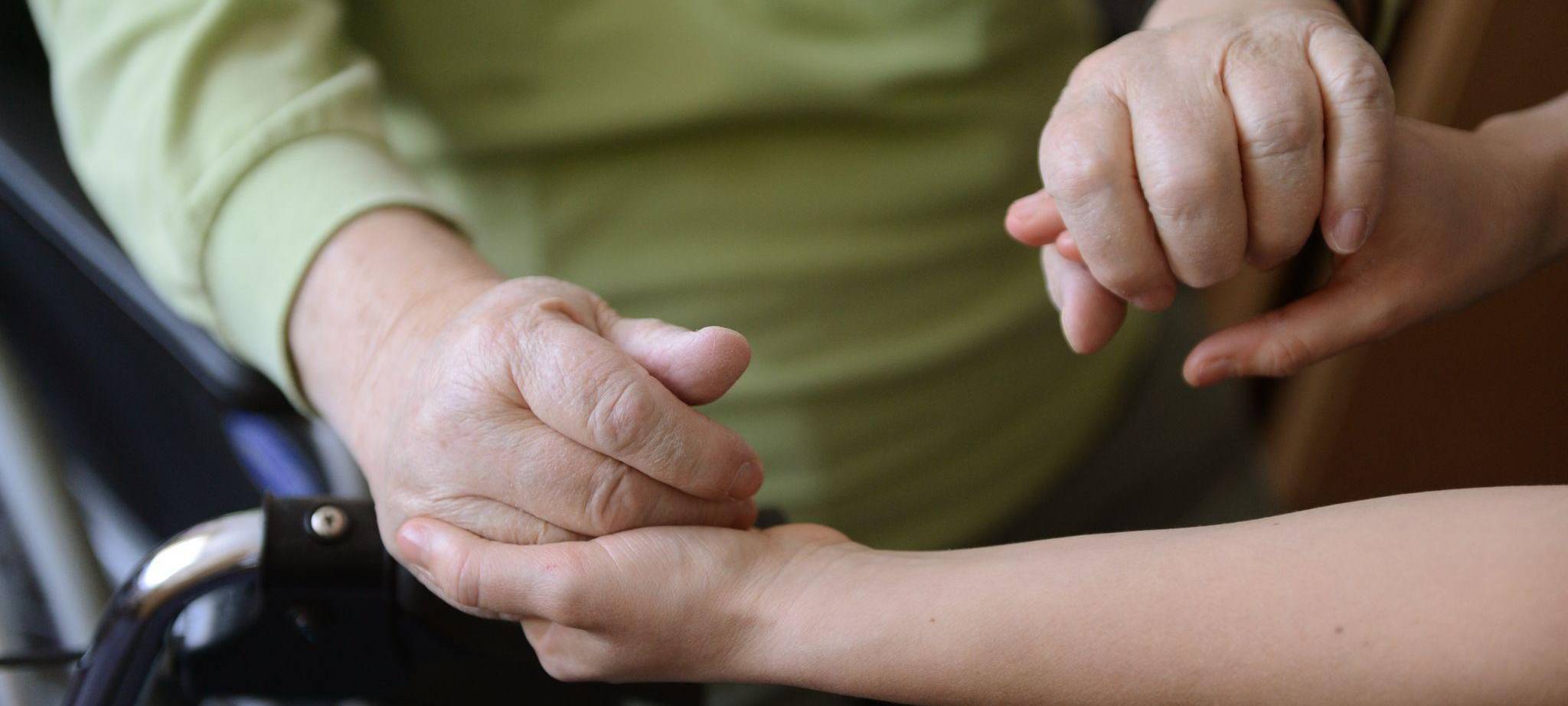 Eine junge Frau hält die Hände eines alten Mannes