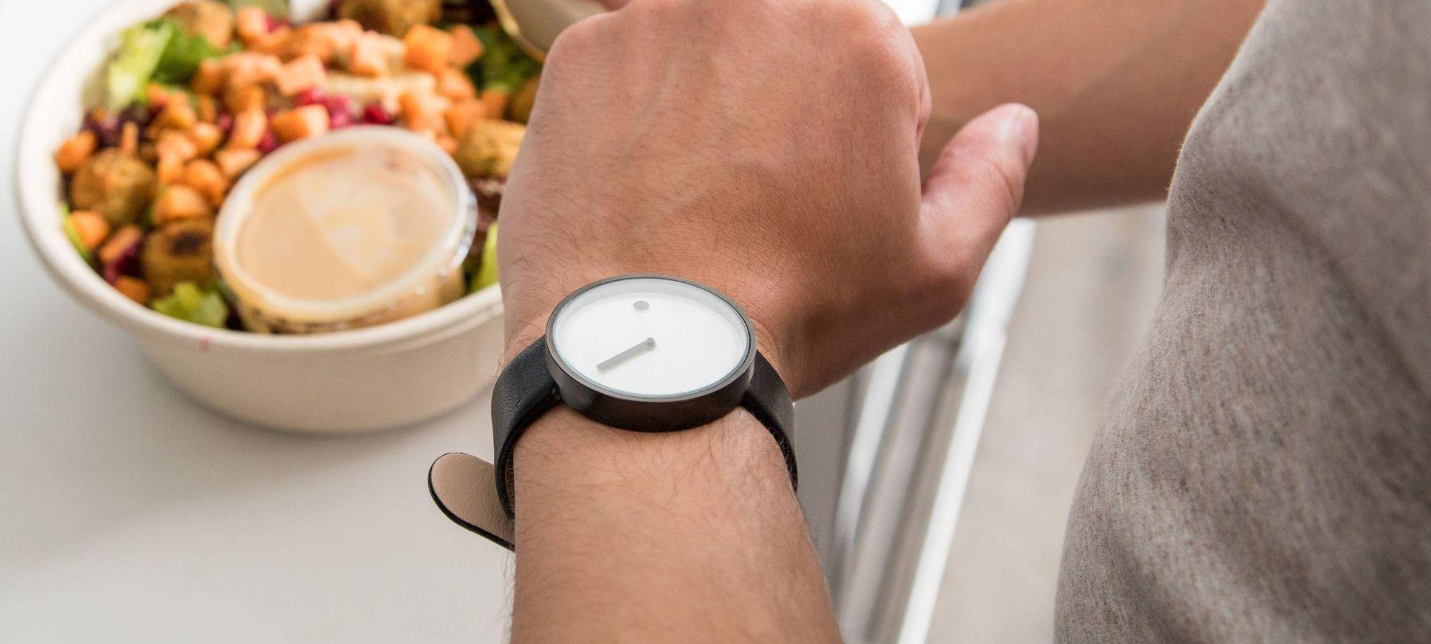 Ein Mann mit einem Teller in der Hand sieht auf seine Uhr