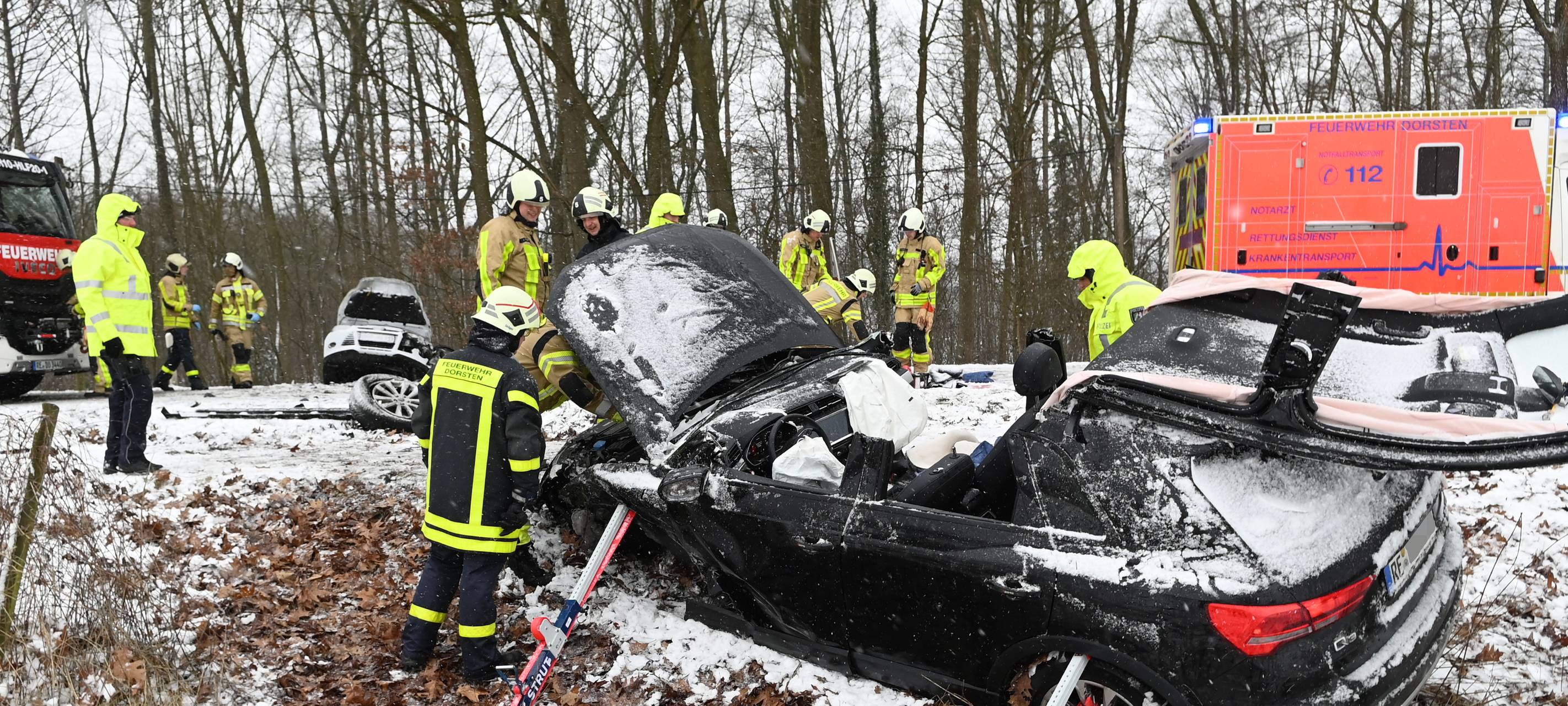 Ein Schwarzes Auto liegt im Graben der B224 in Dorsten. Feuerwehrleute sichern das Auto vorm Abrutschen, das Dach wurde geöffnet, um einen Insassen zu befreien. Es liegt Schnee. Im Hintergrund sind Einsatzfahrzeuge und ein weiterer Wagen im Graben.