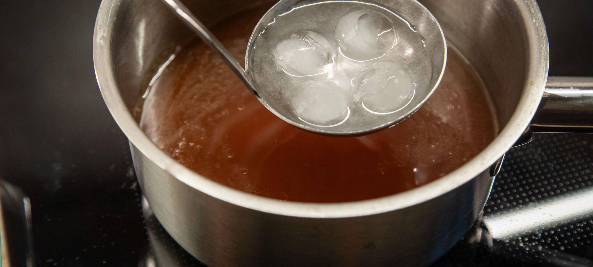 Eis schmilzt in einer Suppenkelle über einer Brühe