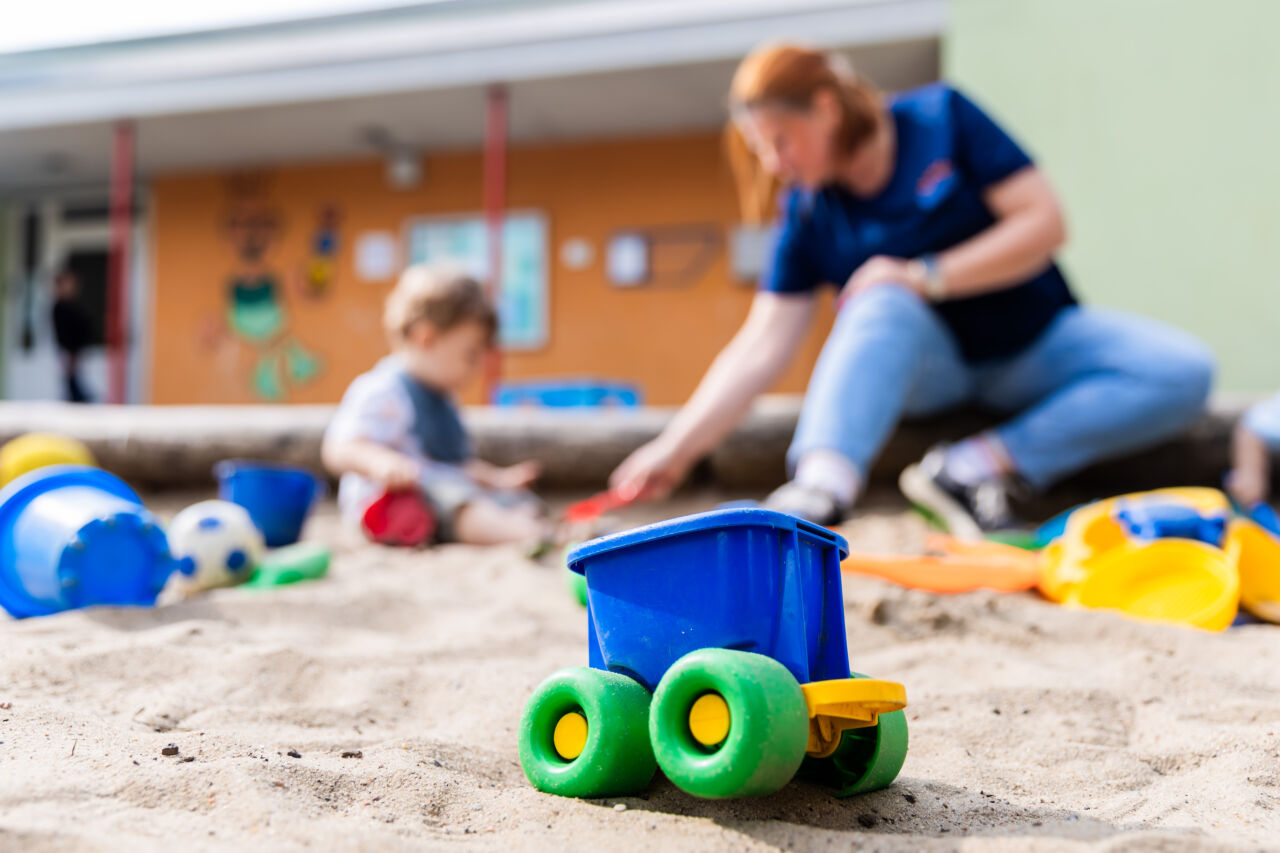 Ein Kind spielt mit einer Erzieherin im Sandkasten einer Kita. 